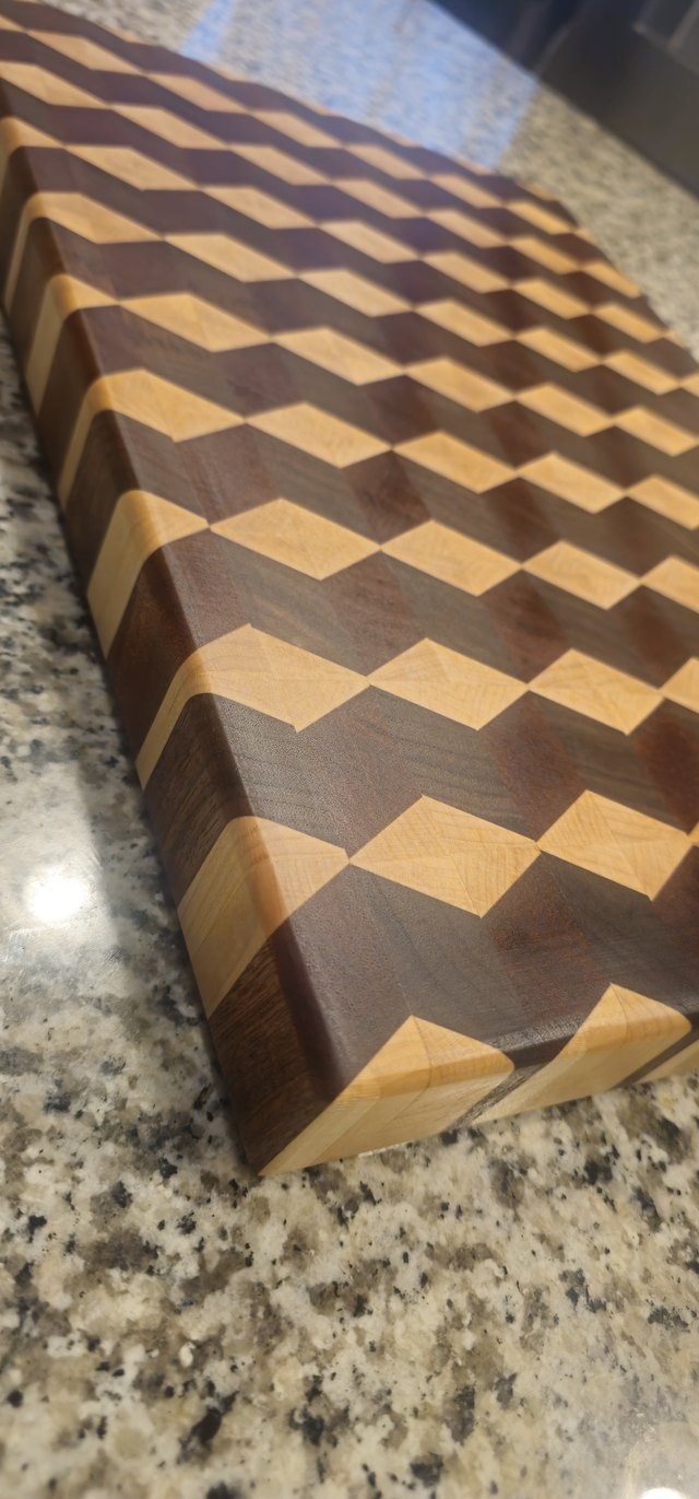 End-grain cutting board with a 3D cube pattern in light and dark woods, on a granite counter